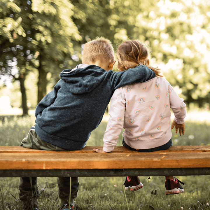 Brother sitting on a park bench with arm around his sister