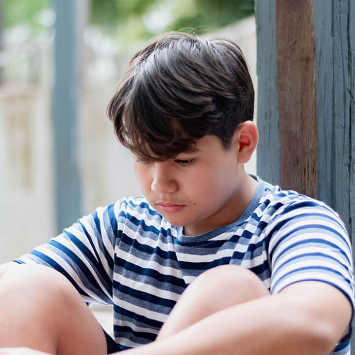Thoughtful young boy sitting alone, reflecting after a bullying incident, symbolizing the need for emotional strength and bullying prevention.