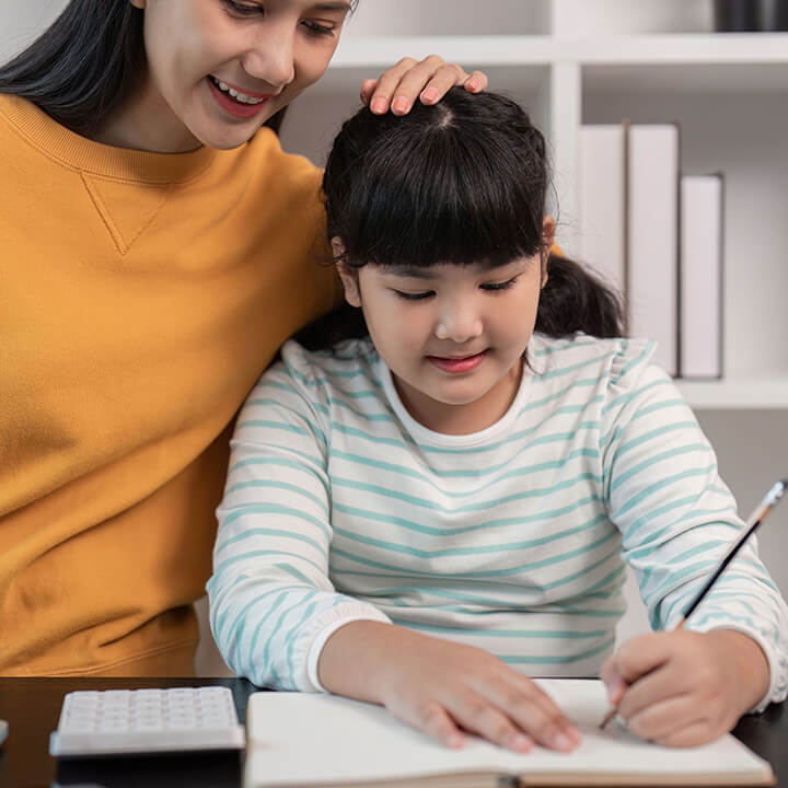 Parent warmly encouraging a child while she works on homework at home, showing empathy and support for learning.