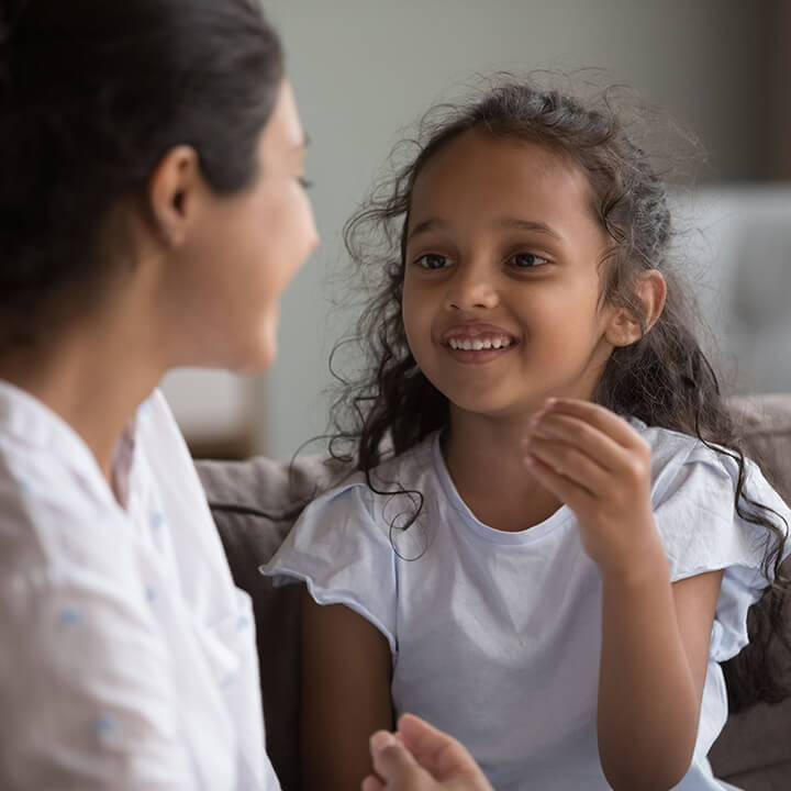 Smiling young girl talking with her mother on the couch, showing heartfelt listening and open communication between parent and child.