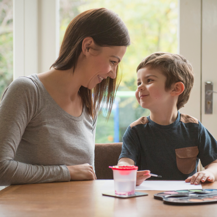 Smiling mother and young son making eye contact while painting, illustrating the power of positive enforceable statements.