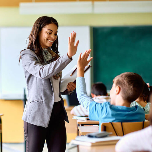 Teacher smiling and high-fiving a student in class, demonstrating empathy, respect, and connection central to building strong relationships with Love and Logic.