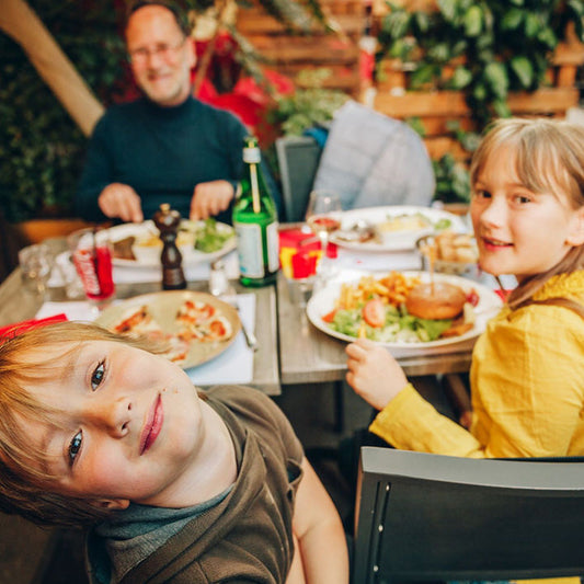 Children learning restaurant manners while eating with family, illustrating courtesy and real-world behavior practice.