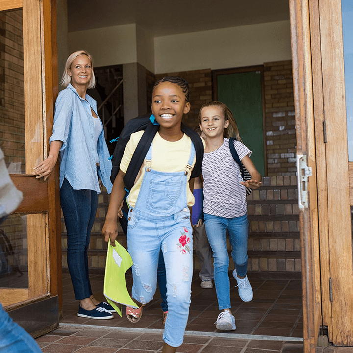 Children happily leaving school with backpacks while a teacher smiles nearby, representing positive relationships and adapting to different teaching styles.