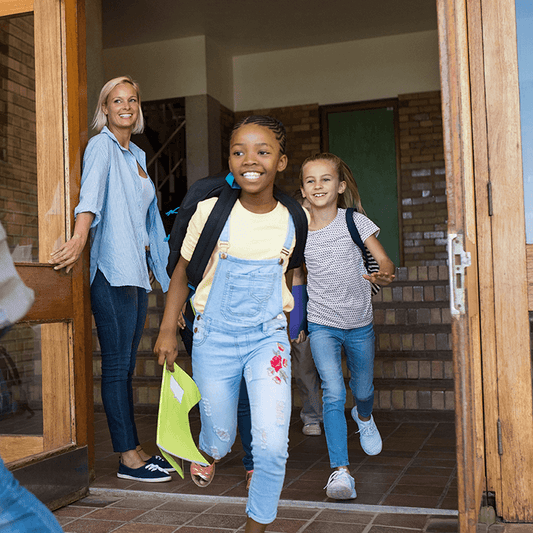 Children happily leaving school with backpacks while a teacher smiles nearby, representing positive relationships and adapting to different teaching styles.