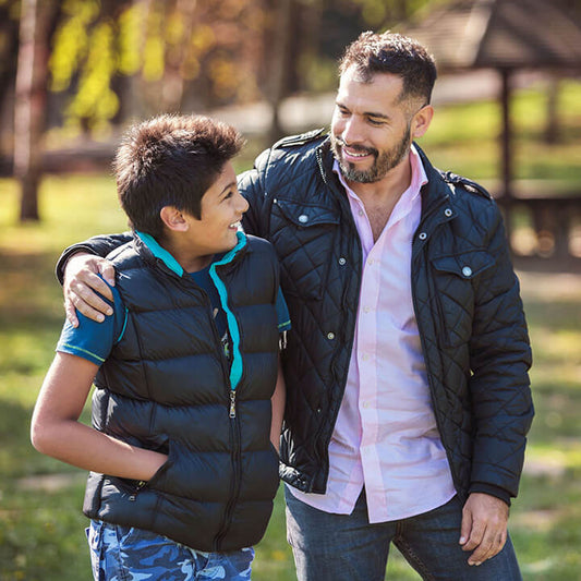 Stepparent and stepchild smiling and walking arm-in-arm outdoors—showing connection, warmth, and trust in their relationship.