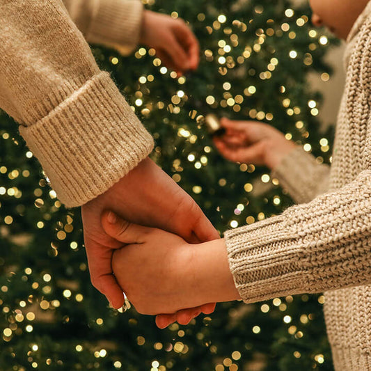 A parent and child holding hands in front of holiday lights, symbolizing connection and love during the holiday season.