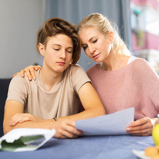 Mother responding calmly to teenage son’s poor grades while reviewing school paper at home