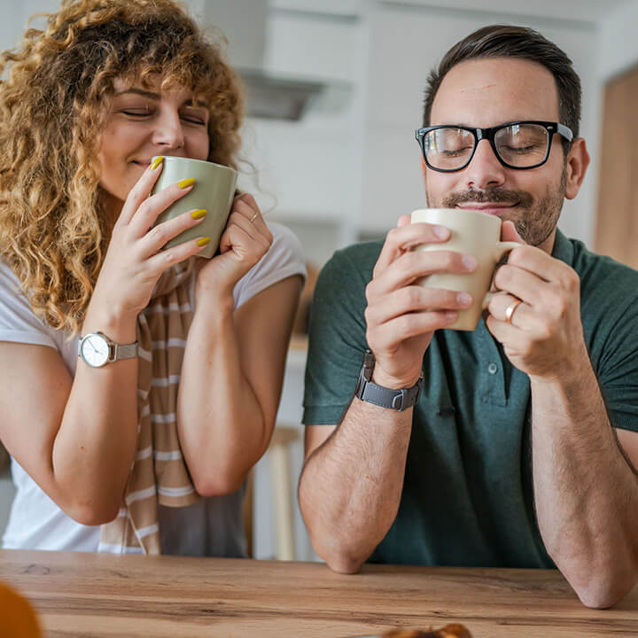 An adult couple sitting together and enjoying warm drinks, expressing calm and relaxation while taking a moment for themselves.