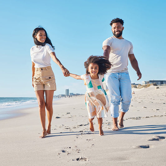 Parents hold hands with their daughter on a sunny beach, representing the Love and Logic parenting process for raising responsible, resilient kids.