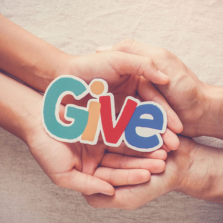 Parent and child hands holding a colorful cutout that says “Give,” symbolizing teaching kids empathy, kindness, and the joy of selflessness.