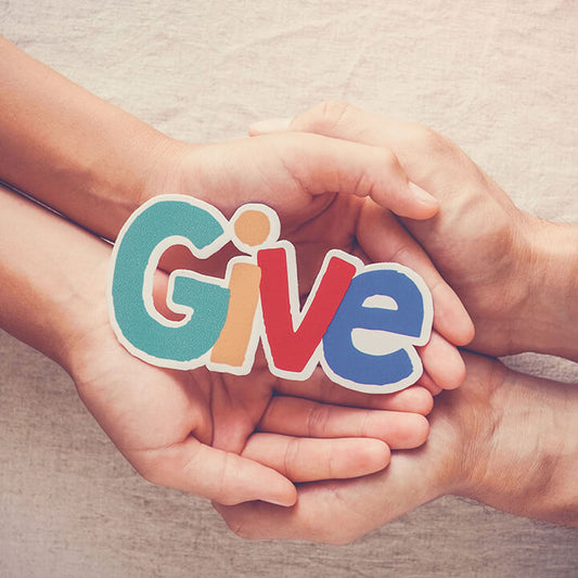 Parent and child hands holding a colorful cutout that says “Give,” symbolizing teaching kids empathy, kindness, and the joy of selflessness.