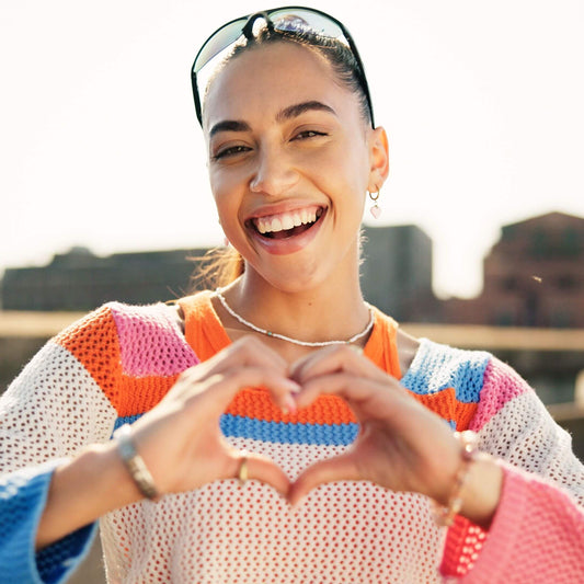 Smiling teacher outdoors forming a heart shape with her hands, symbolizing positivity and self-care.