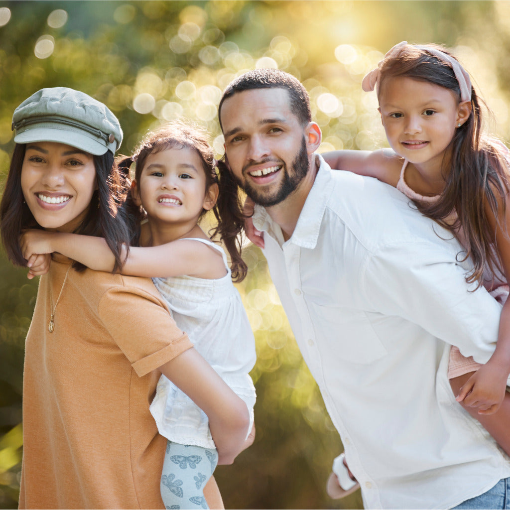 Smiling parents giving their two young daughters piggyback rides outdoors, symbolizing strong family relationships and healthy identity development.